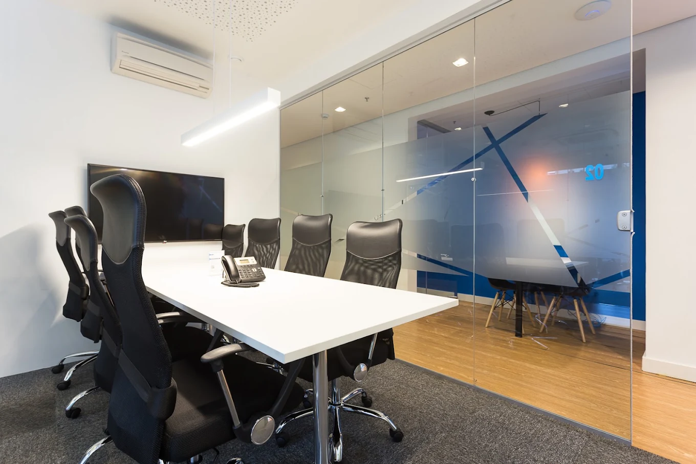 Sala de reunião com mesa branca e divisória de vidro