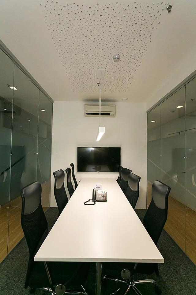 Sala de reunião com mesa branca, cadeiras e tela