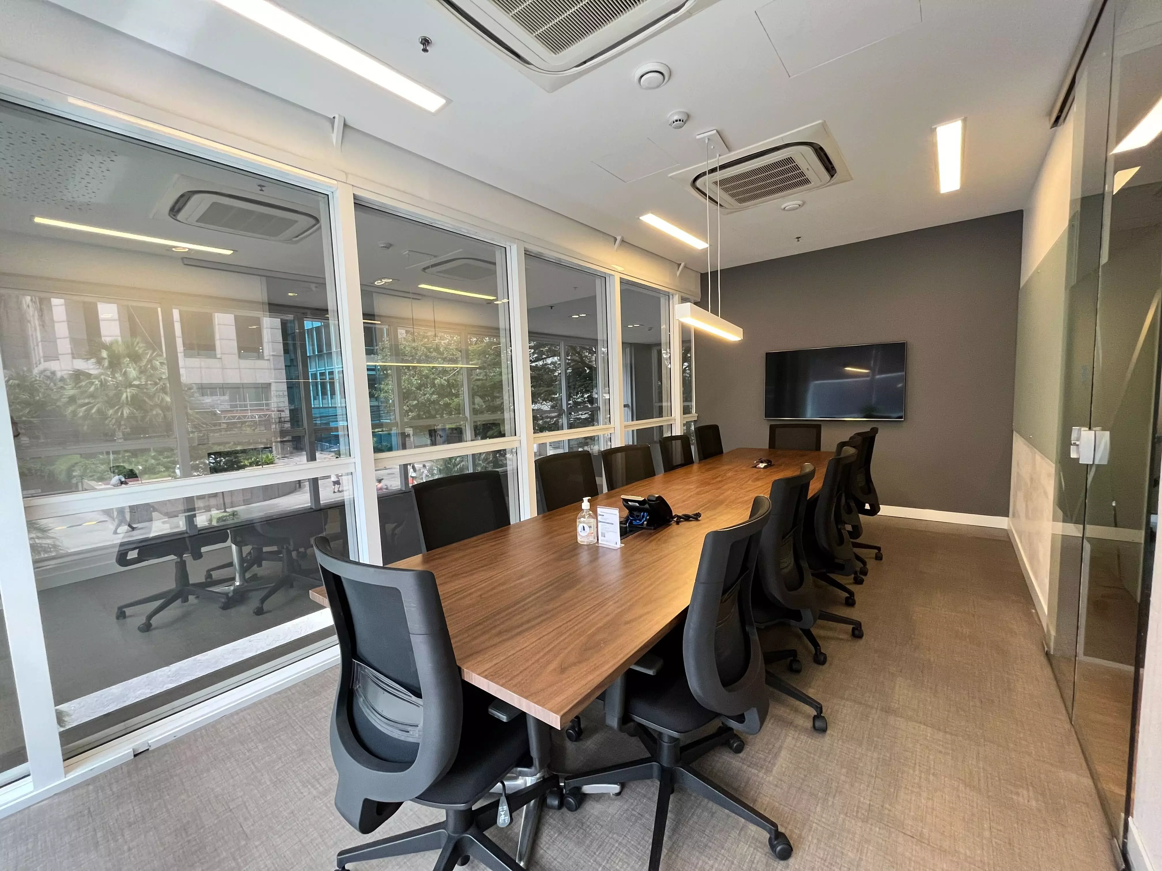 Sala de reunião com mesa de madeira, cadeiras e janelas